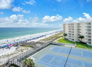 A beachfront property with a tennis court, beach umbrellas, and a building with balconies. - (621) Gulf-Front Condo on 6th Floor, Sleeps 6, Kings, FREE Beach Service (Destin)