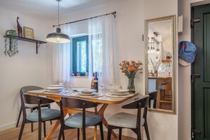 Ein Essbereich mit einem Holztisch, gedeckt für vier Personen, einer Pendelleuchte, einem Fenster mit Vorhängen und einem Spiegel an der Wand.