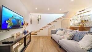 Una sala moderna con televisión de pantalla plana, un sofá, una escalera y una zona de cocina.