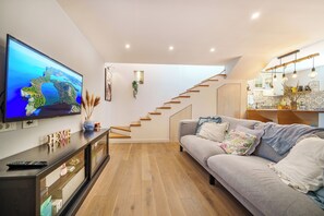 Ein modernes Wohnzimmer mit Flachbildfernseher, einer Couch, einer Treppe und einer Küchenzeile.