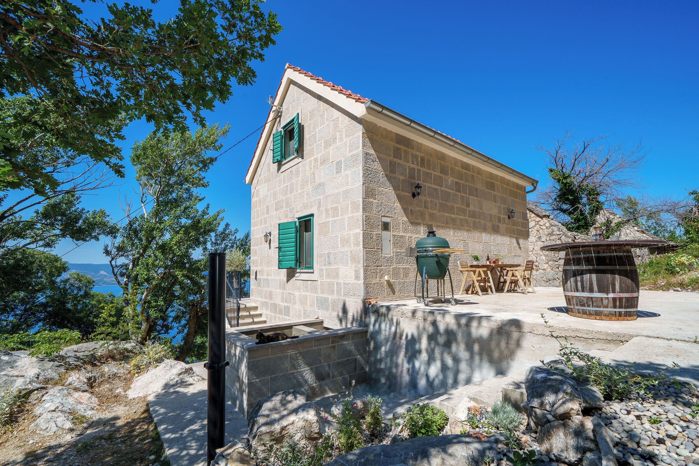 A stone building with a sloped roof, a small porch, and a view of the sea.