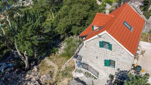 Un edificio de piedra con techo rojo, contraventanas verdes y un balcón con barandilla de metal.