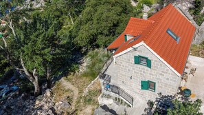 Ein Steinhaus mit rotem Dach, grünen Fensterläden und einem Balkon mit Metallgitter.