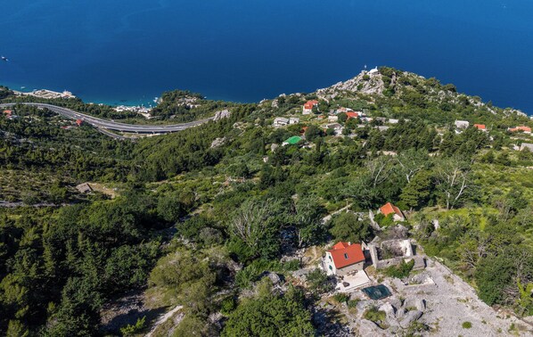 Un paysage montagneux, avec une route sinueuse, des maisons éparpillées et une étendue d’eau visible au loin.