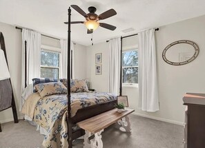 Une chambre à coucher avec un lit à baldaquin, un ventilateur de plafond, une table de chevet et une fenêtre avec des rideaux.