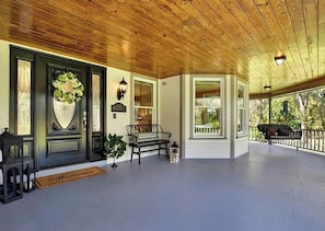 Eine überdachte Veranda mit einer Bank, einer Tür mit einem Kranz und einer Fußmatte.