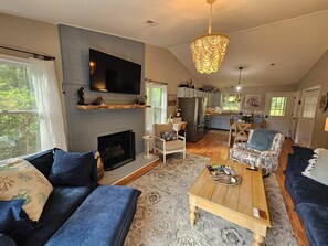 A living room with a fireplace, a television, and a dining area with a kitchen in the background. - Waterfront Retreat with Private Dock (Heathsville)