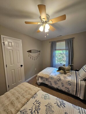 Ein Schlafzimmer mit zwei Betten, einem Deckenventilator, einem Fenster mit Vorhängen und einer Wanddekoration.