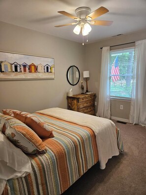 A bedroom with a bed, a ceiling fan, a window with curtains, a dresser, and a painting on the wall. - Waterfront Retreat with Private Dock (Heathsville)