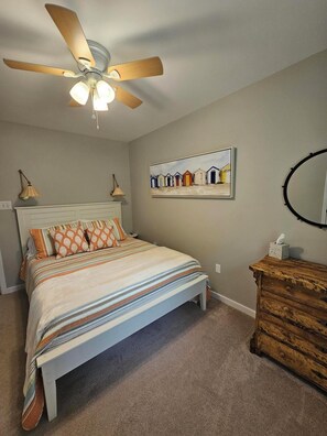 A bedroom with a bed, a ceiling fan, a bedside table, a dresser, a framed picture on the wall, and a round mirror. - Waterfront Retreat with Private Dock (Heathsville)
