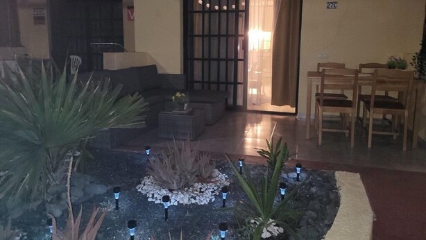 Un espacio interior acogedor con una zona de estar, un pequeño jardín con plantas e iluminación decorativa, y una puerta que da a otra habitación.