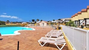 Una piscina con sillones de descanso y un flotador salvavidas, rodeada por un suelo de baldosas y edificios.