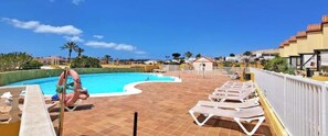 Ein Schwimmbecken mit Liegestühlen und einem Rettungsring, umgeben von einer gefliesten Terrasse und Gebäuden.