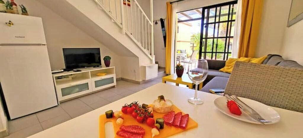 A dining area with a table set for two, a television, and a staircase leading to an upper level.
