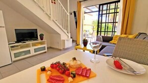 Un comedor con una mesa lista para dos personas, un televisor y una escalera que sube a un nivel superior.