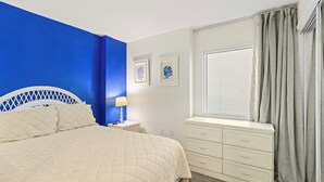 A bedroom with a bed, a nightstand, a dresser, a window with curtains, and two wall-mounted pictures. - 2BR Beachfront corner condo w private beach & hot tub ~ Sleeps 8 (Gulf Shores)