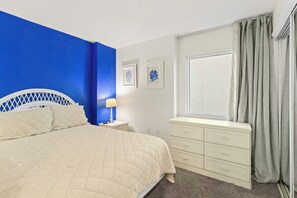 A bedroom with a bed, a nightstand, a dresser, a window with curtains, and two wall-mounted pictures. - 2BR Beachfront corner condo w private beach & hot tub ~ Sleeps 8 (Gulf Shores)