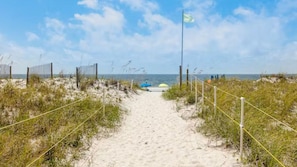 A sandy beach path with a flag, leading to the sea. - 2BR Beachfront corner condo w private beach & hot tub ~ Sleeps 8 (Gulf Shores)