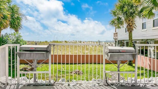 A gated outdoor area with two barbecue grills, a grassy lawn, and a building in the background. - 2BR Beachfront corner condo w private beach & hot tub ~ Sleeps 8 (Gulf Shores)