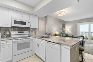 A modern kitchen with white cabinetry, a built-in oven, a microwave, and a dishwasher. - 2BR Beachfront corner condo w private beach & hot tub ~ Sleeps 8 (Gulf Shores)