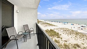 Ein Balkon mit zwei Stühlen und Blick auf einen Strand mit Sonnenschirmen und Menschen.