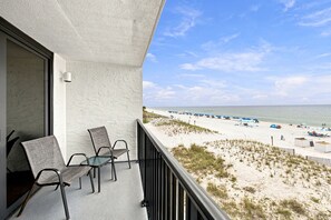 Ein Balkon mit zwei Stühlen und Blick auf einen Strand mit Sonnenschirmen und Menschen.