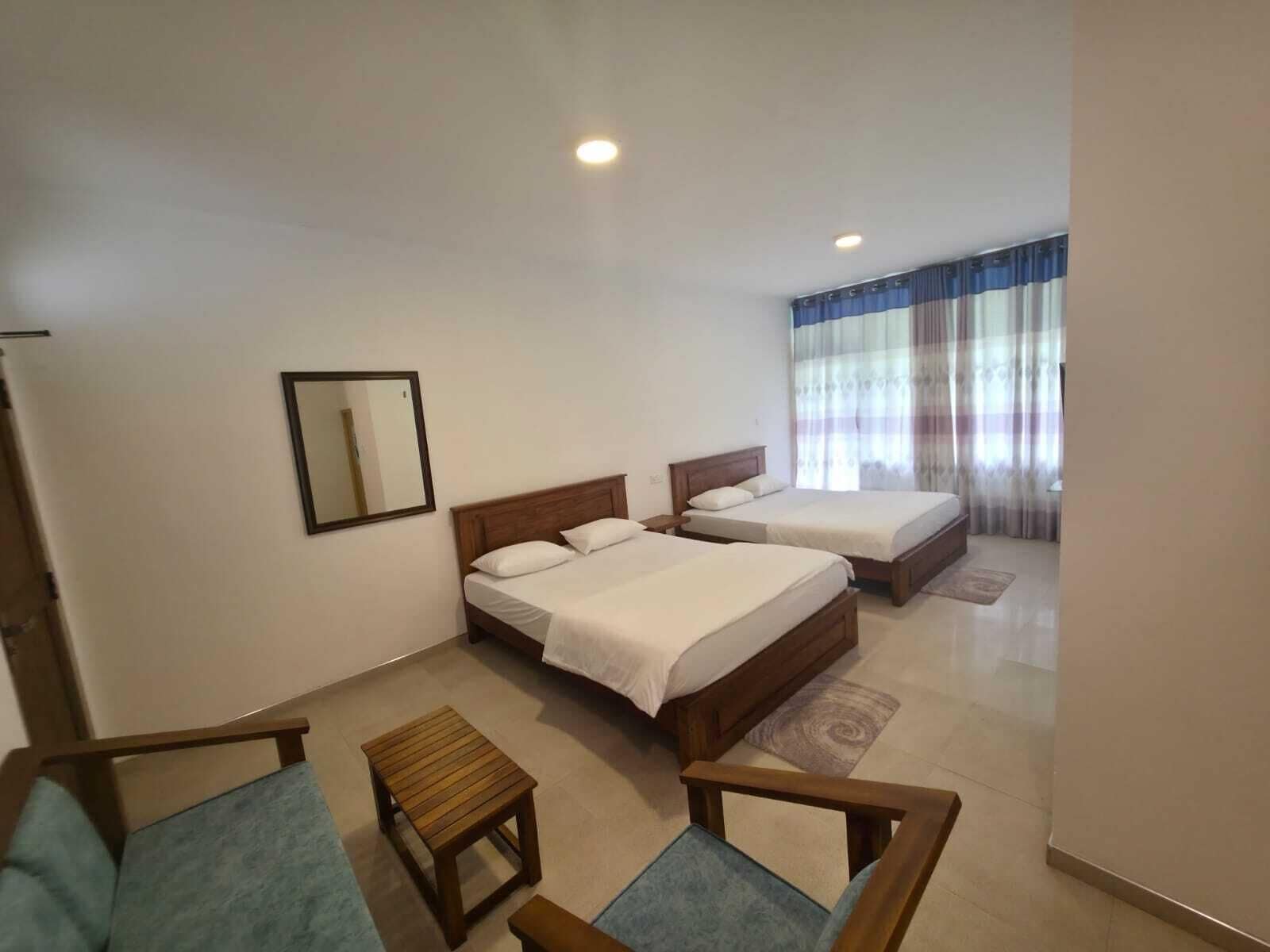 Una camera d'albergo con due letti, un tavolino, una sedia, uno specchio e una finestra con tende.
