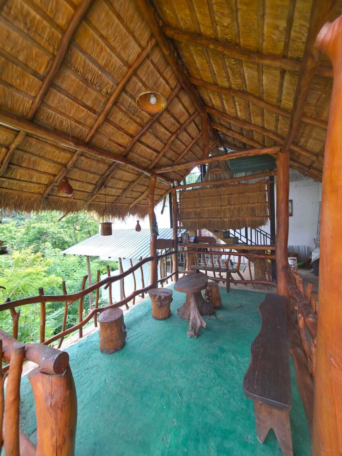 Estructura de techo de paja con muebles de madera y suelo verde, rodeada por una valla de madera.