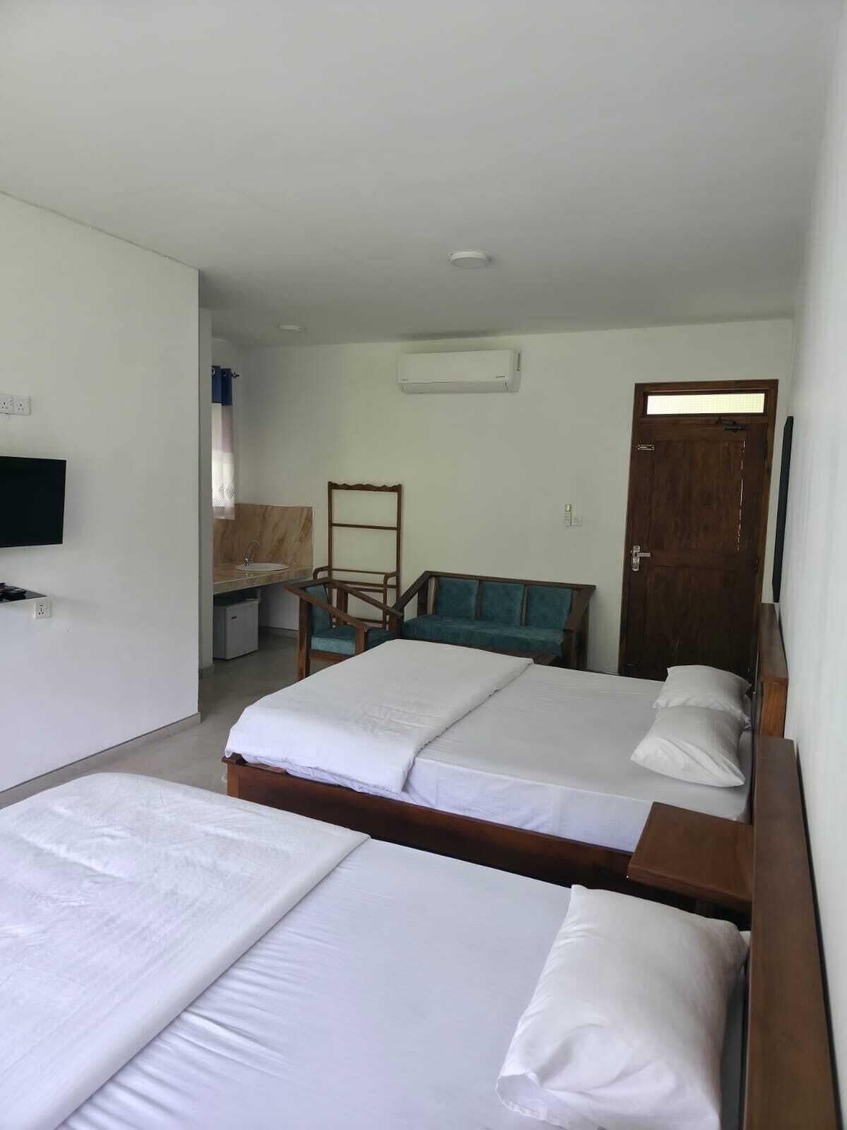 A hotel room with two beds, a desk, a chair, a television, and an air conditioning unit.