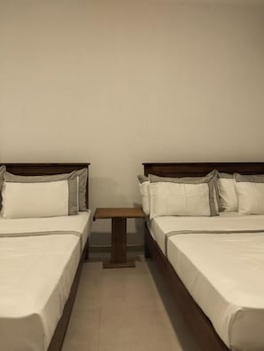 Una habitación con dos camas, una mesita pequeña y paredes lisas.