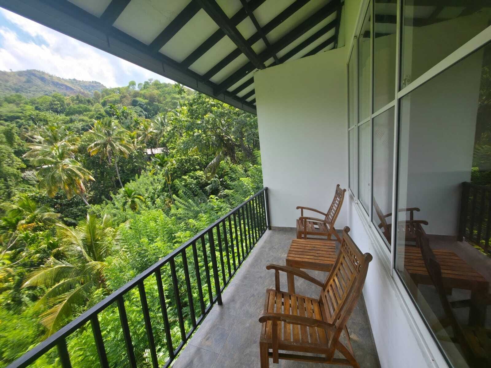 Un balcone con sedie e tavolo in legno, affaccia su un paesaggio verdeggiante con palme e una montagna all'orizzonte.