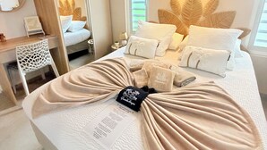 Quarto de hotel com cama, escrivaninha, cadeira, espelho e luminária na parede.