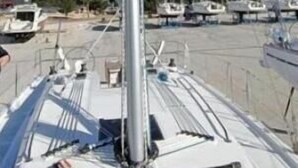O mastro e a aparelhagem de um veleiro, com um porto de recreio ao fundo.