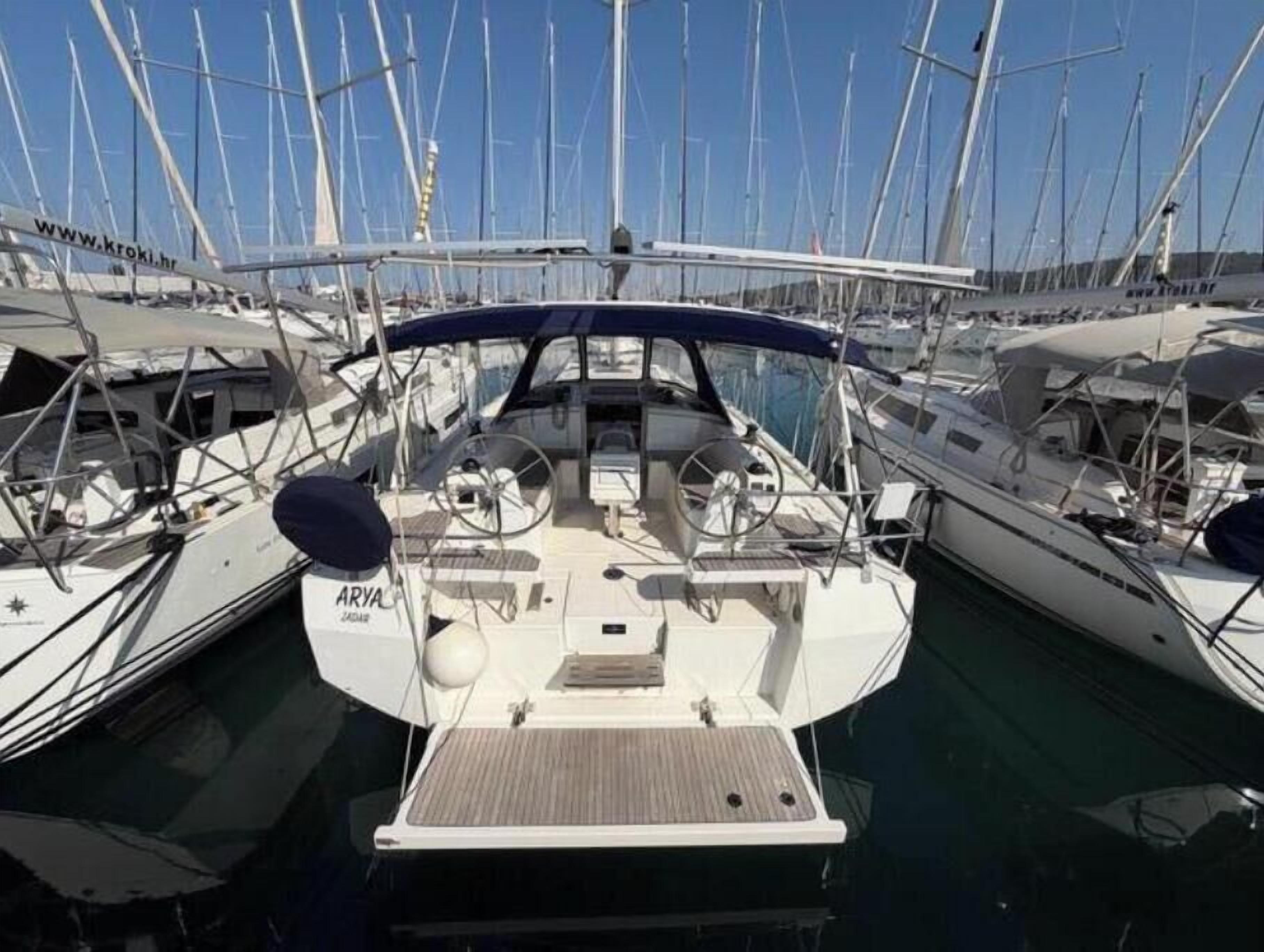 A marina with multiple sailboats docked, featuring a central boat with a covered deck and a name 'ARYAL' visible.