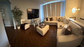 A modern living room with a sectional sofa, a flat-screen TV, a coffee table, and a potted plant. - Elegance, tranquility, and comfort. Close to everything. (Schenectady)