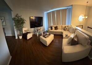 Ein modernes Wohnzimmer mit einem Ecksofa, einem Flachbildfernseher, einem Couchtisch und einem Topf mit Pflanze.