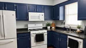 A kitchen with dark blue cabinets, white appliances, a black countertop, and a wooden floor. - Elegance, tranquility, and comfort. Close to everything. (Schenectady)
