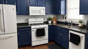 A kitchen with dark blue cabinets, white appliances, a black countertop, and a wooden floor.