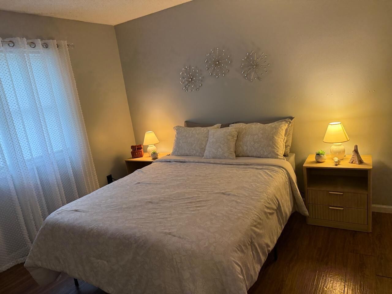 Een slaapkamer met een bed, twee nachtkastjes, een lamp en decoratieve wandkunst.