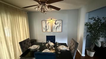 Een eetruimte met een tafel voor vier personen, een plafondventilator en twee abstracte kunstwerken aan de muur.