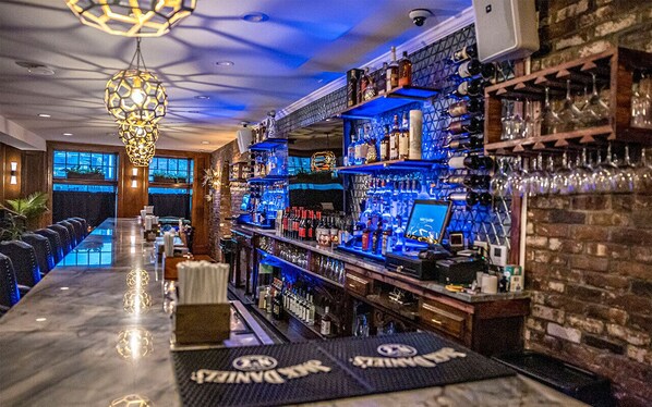 A bar area with a long counter, shelves with bottles, and a hanging light fixture. - Elegance, tranquility, and comfort. Close to everything. (Schenectady)