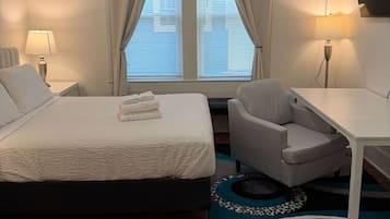 A hotel room with a bed, a desk, a chair, a TV, and a window with curtains.