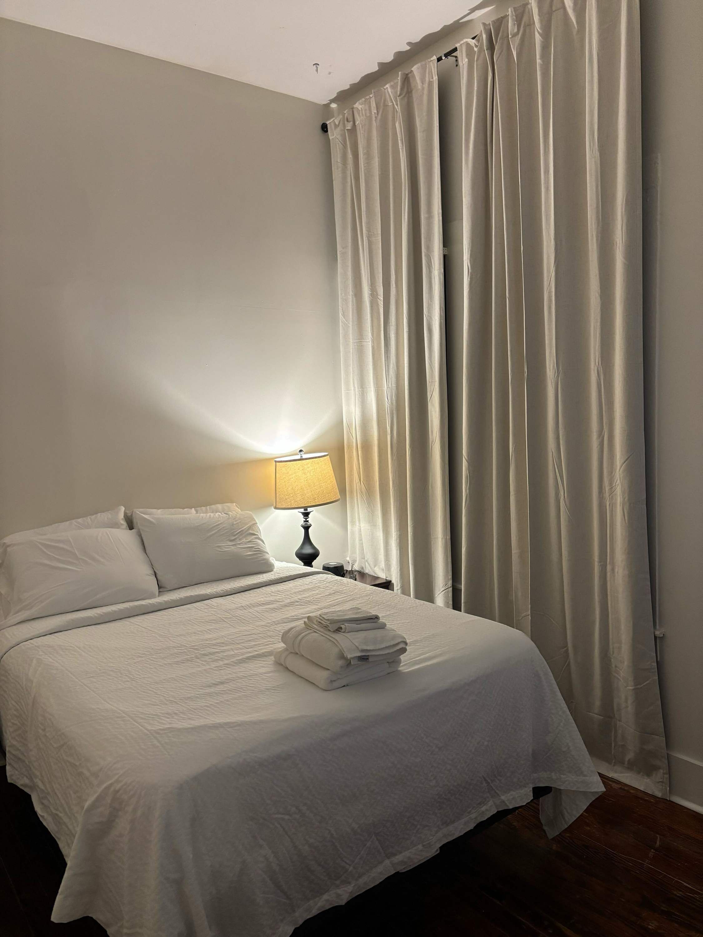 A hotel room with a bed, a nightstand with a lamp, and a window with curtains.