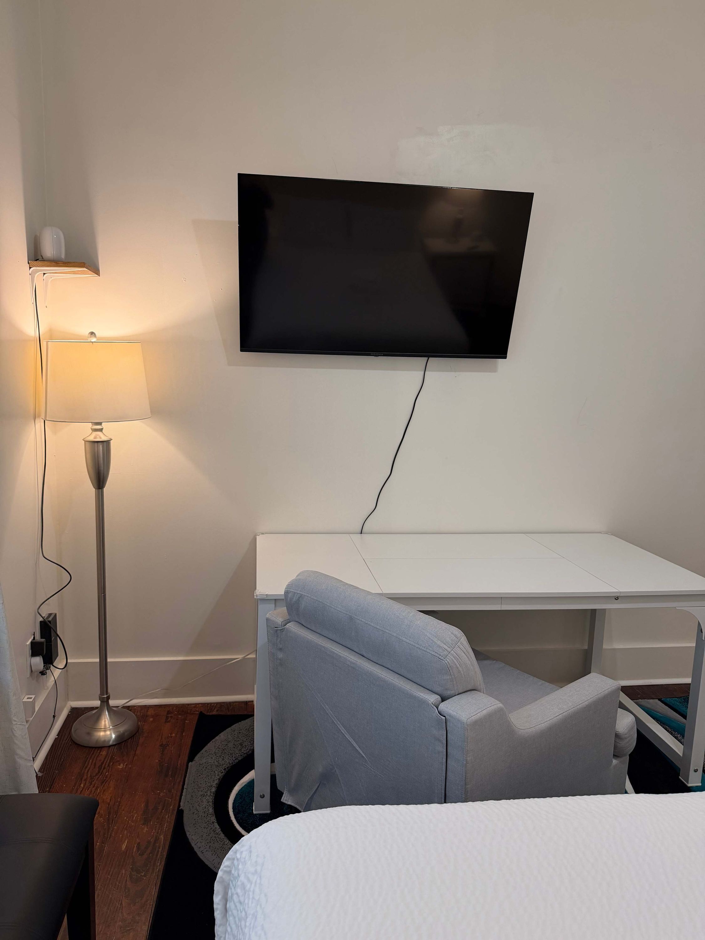 Hotellihuone, jossa on seinälle asennettu taulutelevisio, työpöytä, tuoli, sänky ja lattiavalaisin.