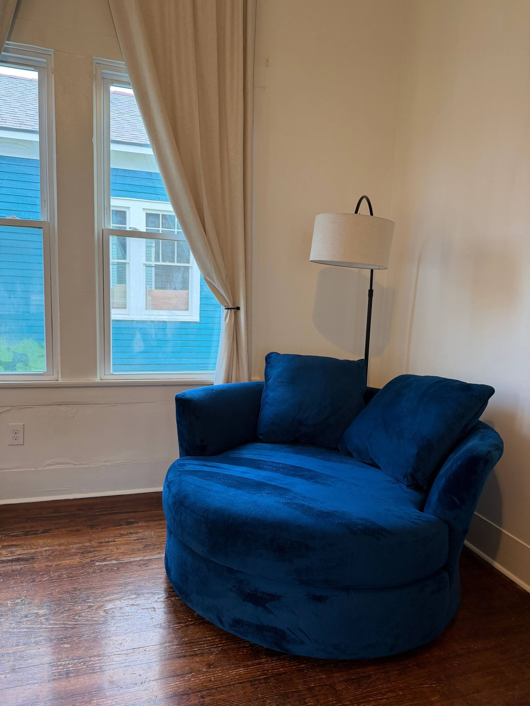A room with a blue armchair, a floor lamp, and a window with curtains.