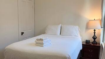 A neatly made bed with white linens, a bedside table with a lamp, and a bench in front of the bed.
