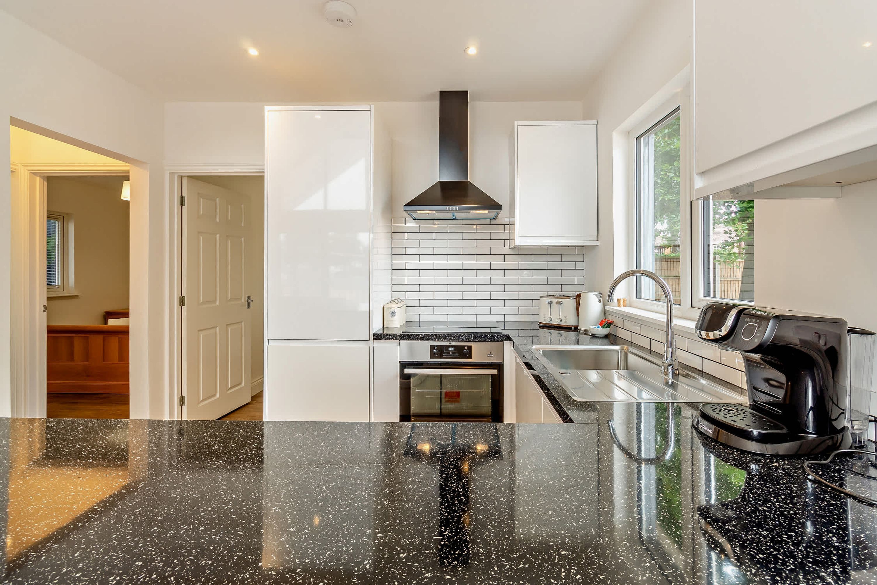 A modern kitchen with white cabinets, a black countertop, a stainless steel range hood, and a coffee maker.