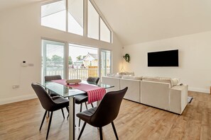 Ein modernes Wohnzimmer mit einem Glastisch, schwarzen Stühlen, einer Couch und einem an der Wand befestigten Flachbildfernseher.