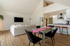 A modern kitchen with white cabinets, a black range hood, and a dining area with a glass table and black chairs. - Host Stay Robin Lodge (Great Yarmouth)
