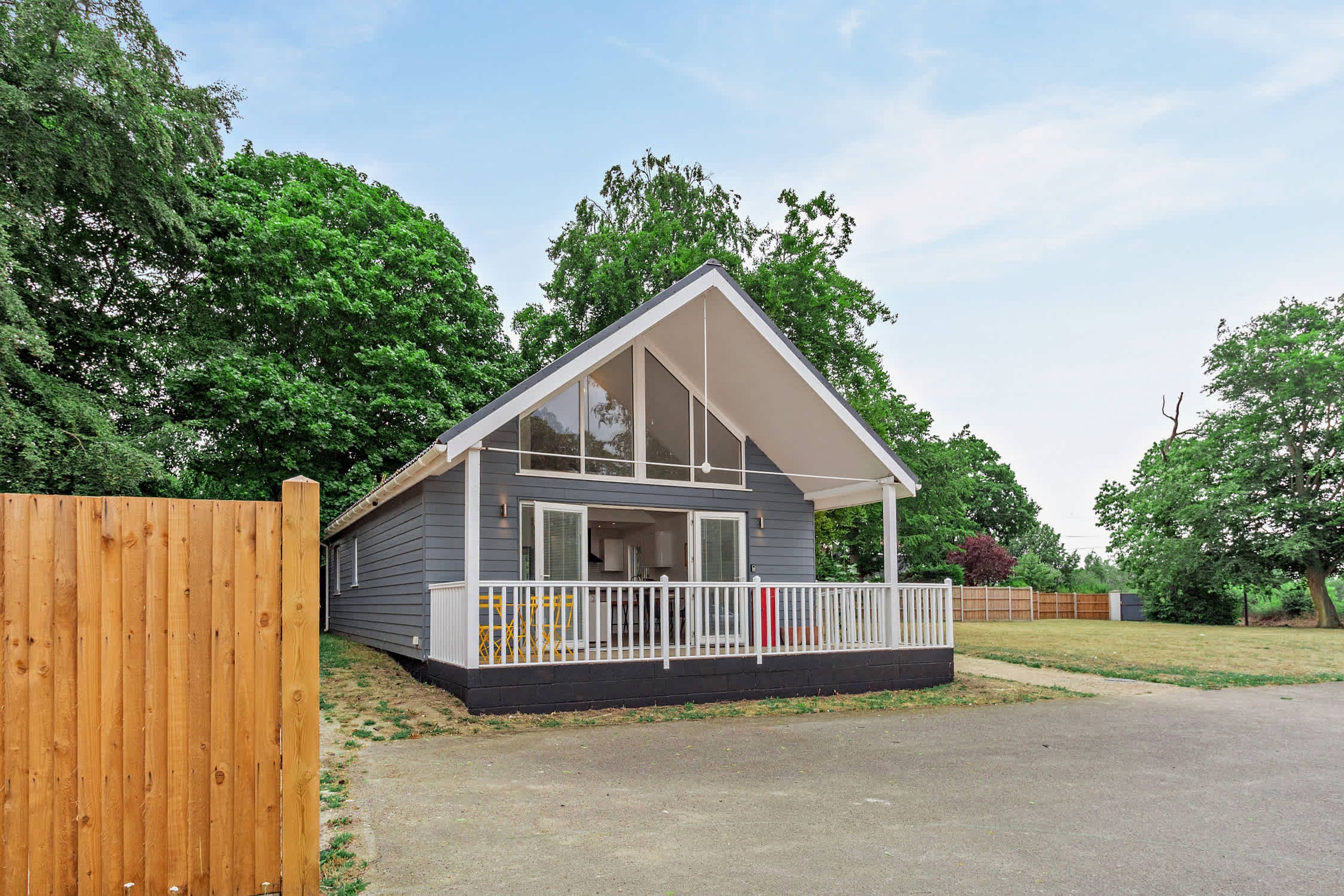 A single-story house with a gabled roof, a front porch with a white railing, and a wooden fence to the left.